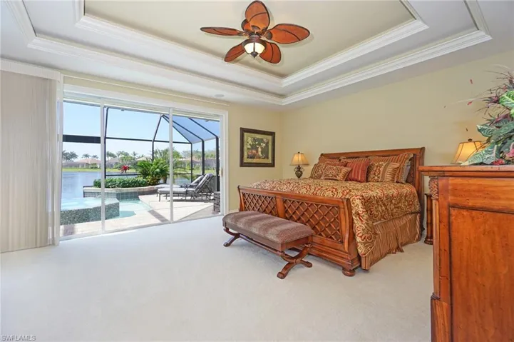 Bedroom featuring a tray ceiling, light colored carpet, a water view, a sunroom, and access to outside