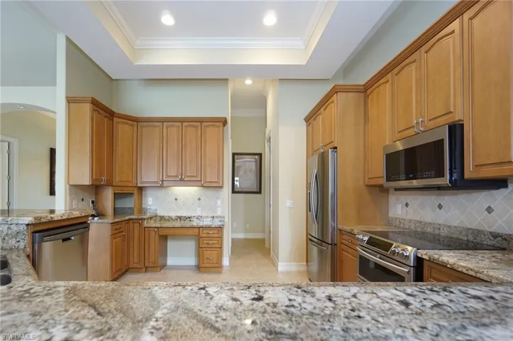 Kitchen featuring backsplash, crown molding, appliances with stainless steel finishes, light stone counters, and a raised ceiling