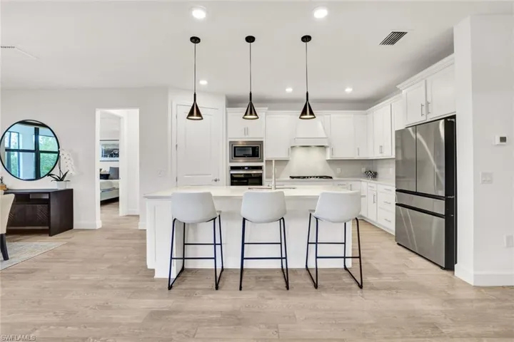 Kitchen with stainless steel appliances, white cabinetry, a breakfast bar area, an island with sink, and decorative light fixtures