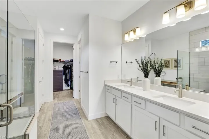 Master ensuite bathroom featuring a frameless shower, double vanity with square sinks and quartz countertops, a spacious walk-in closet  and light colored tile floors