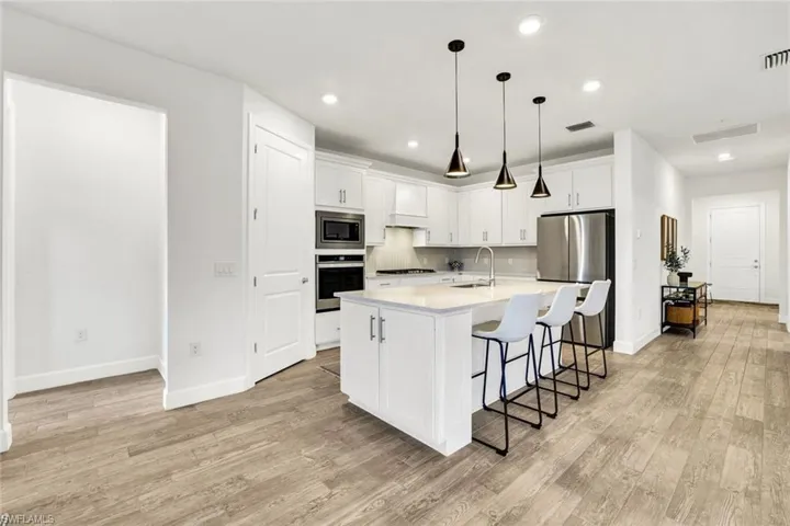 Kitchen with a center island with sink, breakfast bar, decorative light fixtures, stainless steel appliances and white cabinets