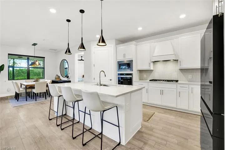 Kitchen with stainless steel appliances, gas range with hood, pendant lighting, white cabinetry, and a kitchen island with sink