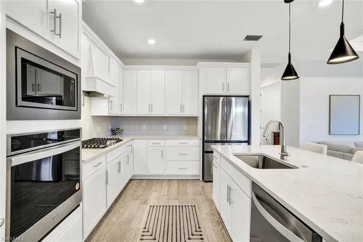 Kitchen featuring stainless steel appliances, white cabinetry, quartz countertops, built in oven and microwave and light tile flooring