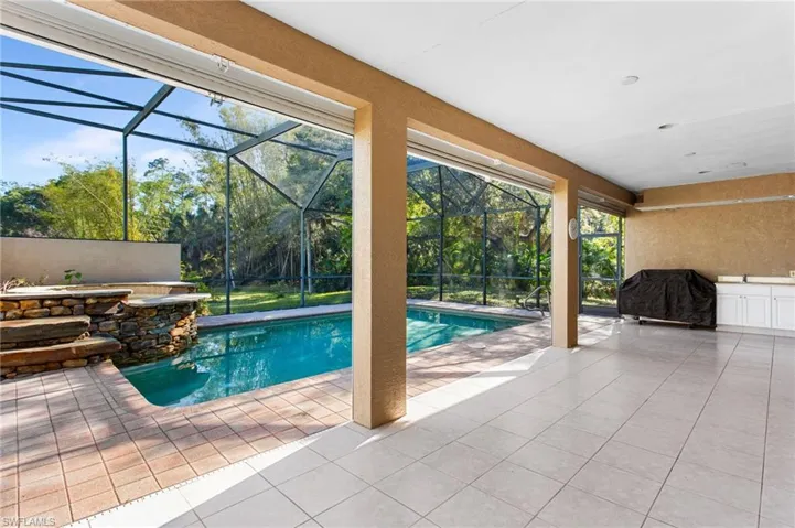 Screened lanai featuring a swimming pool with a stone waterfall, a tiled patio area, and an outdoor kitchen with white cabinetry