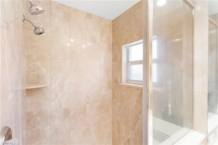 Shower with light-toned tiled walls, dual showerheads, and a built-in corner shelf