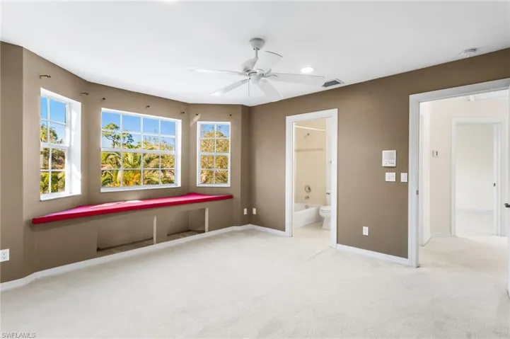 Spacious room featuring a bay window with a built-in window seat, neutral carpeting, a ceiling fan, and direct access to an adjacent bathroom with a tub and shower