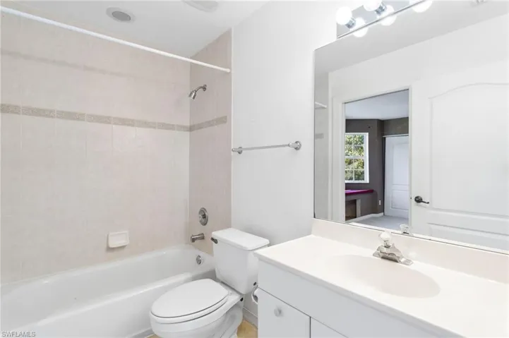 Full bathroom featuring a white vanity with integrated sink, rectangular mirror with overhead lighting, a toilet, and a bathtub with tiled surround and shower fixture