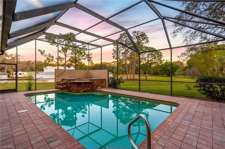 Screened outdoor pool area featuring a rectangular pool, integrated stone-clad spa, and brick paver decking
