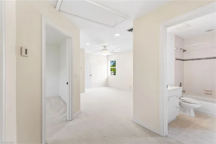 Light-filled interior featuring neutral wall tones, carpeted flooring, a ceiling fan, and a window with green outdoor scenery