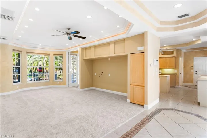 Spacious carpeted room featuring a bay window, recessed lighting, ceiling fan, and tray ceilings