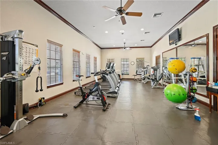 Spacious fitness center featuring neutral walls, dark trim, multiple windows with blinds, ceiling fans, and impact-absorbing flooring