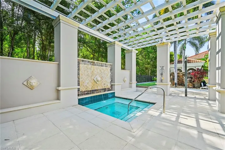 Spa area featuring a tiled water feature, a white pergola, and light-toned paving