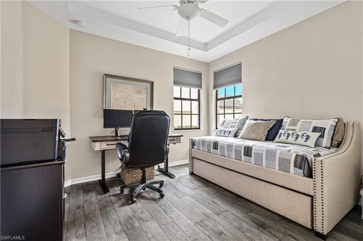 Tray ceiling with a ceiling fan, two windows with blinds, and wood-finish flooring