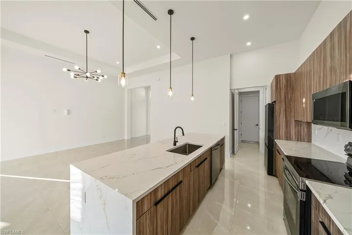 Kitchen featuring stainless steel appliances, light stone counters, modern cabinets, wood finish cabinetry, and a raised ceiling