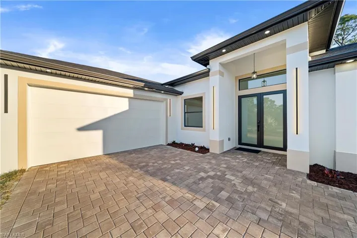 Doorway to property with french doors, decorative driveway, stucco siding, and a garage
