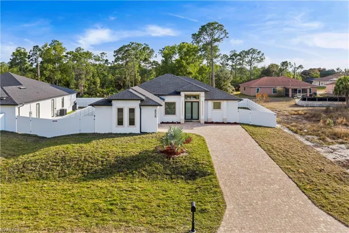 View of front facade featuring a gate, decorative driveway, stucco siding, view of wooded area, and roof with shingles
