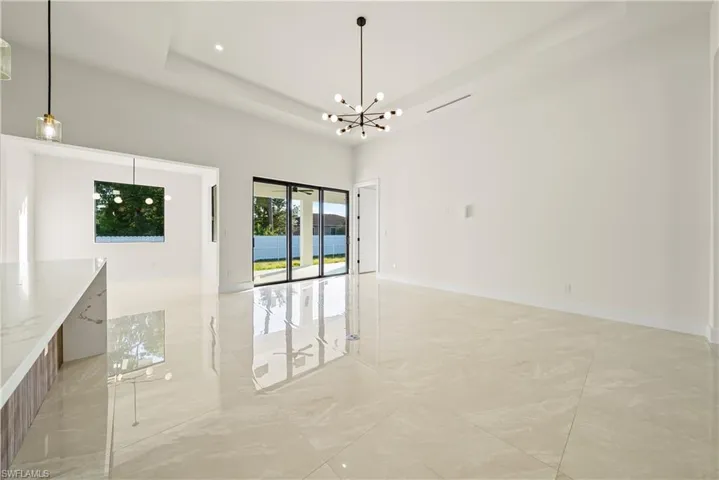 Spare room featuring a raised ceiling, a chandelier, and light marble finish floors