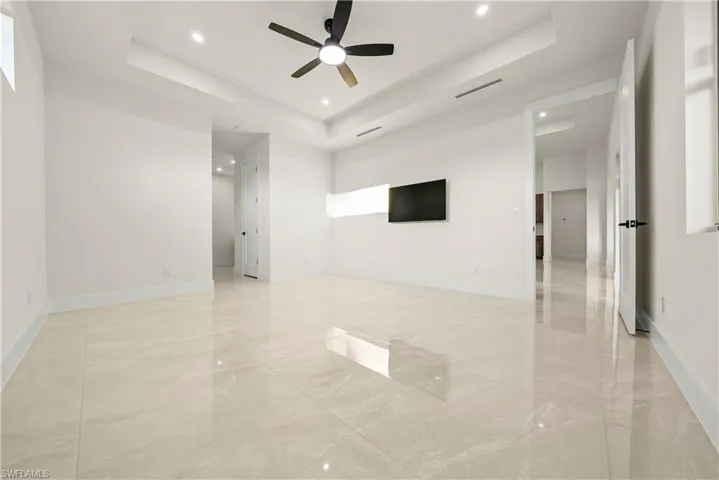 Unfurnished room featuring a tray ceiling, a ceiling fan, recessed lighting, and light marble finish flooring