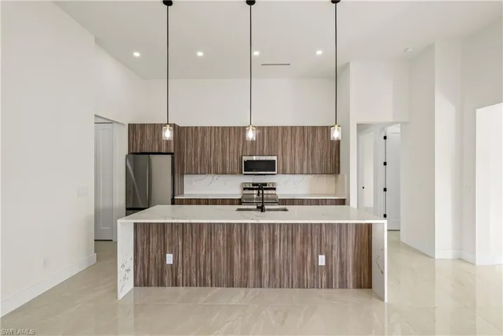 Kitchen featuring light stone countertops, a high ceiling, wood finish cabinets, a kitchen island with sink, and modern cabinets