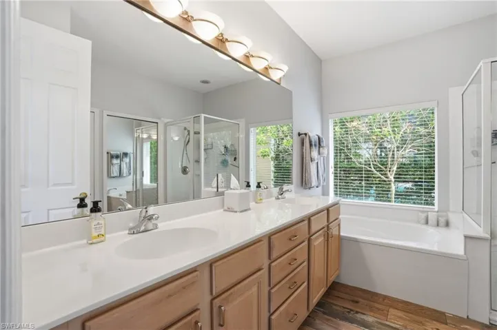 Bathroom featuring a garden tub, a shower stall, double vanity, and dark wood-style floors