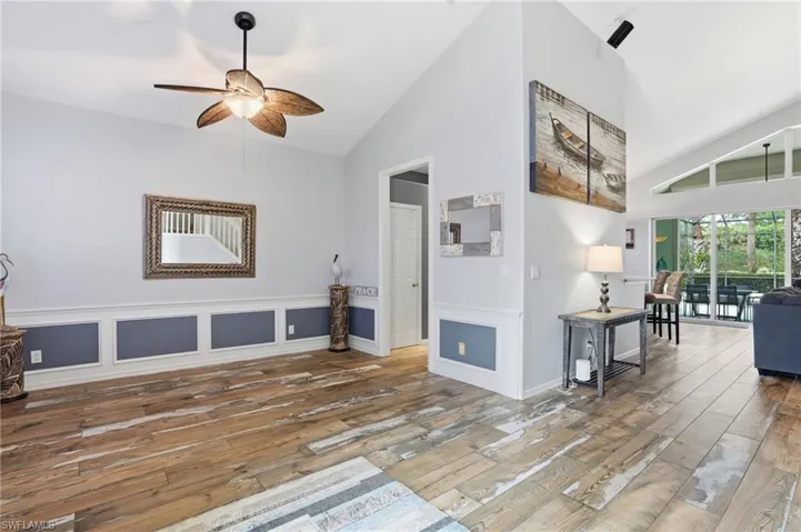 Living room with ceiling fan, lofted ceiling, light wood finished floors, a decorative wall, and a wainscoted wall