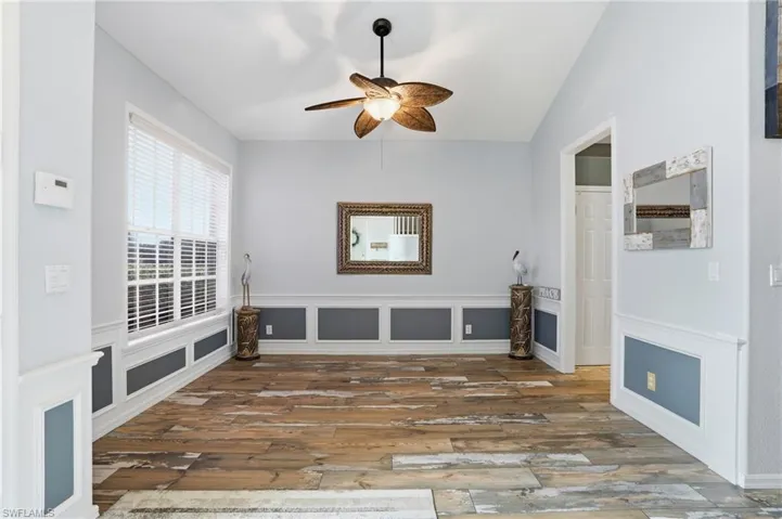 Unfurnished living room with ceiling fan, wood finished floors, a decorative wall, and wainscoting