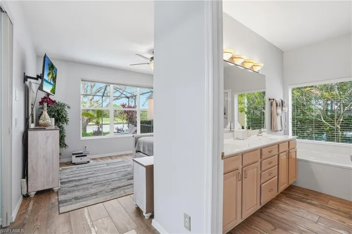 Ensuite bathroom featuring light wood-style flooring, double vanity, ceiling fan, and plenty of natural light