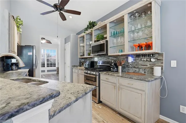 Kitchen featuring stainless steel appliances, light stone counters, vaulted ceiling, light wood finished floors, and decorative backsplash