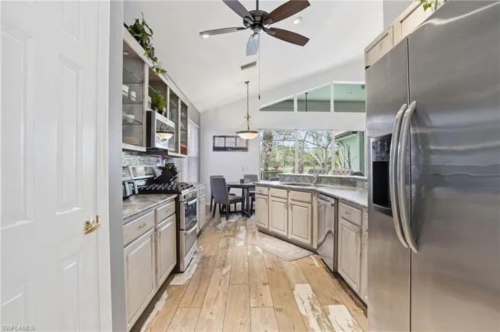 Kitchen with stainless steel appliances, vaulted ceiling, pendant lighting, light wood finished floors, and glass fronted cabinets