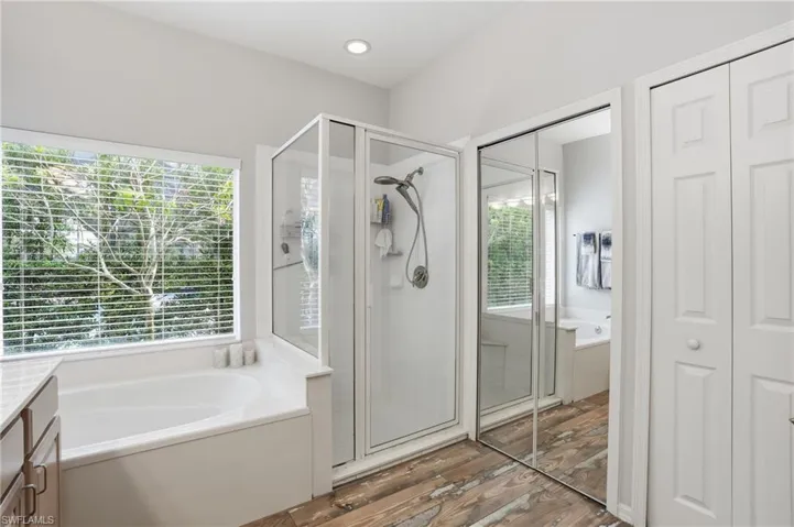 Bathroom with a garden tub, a stall shower, vanity, a closet, and light wood-type flooring
