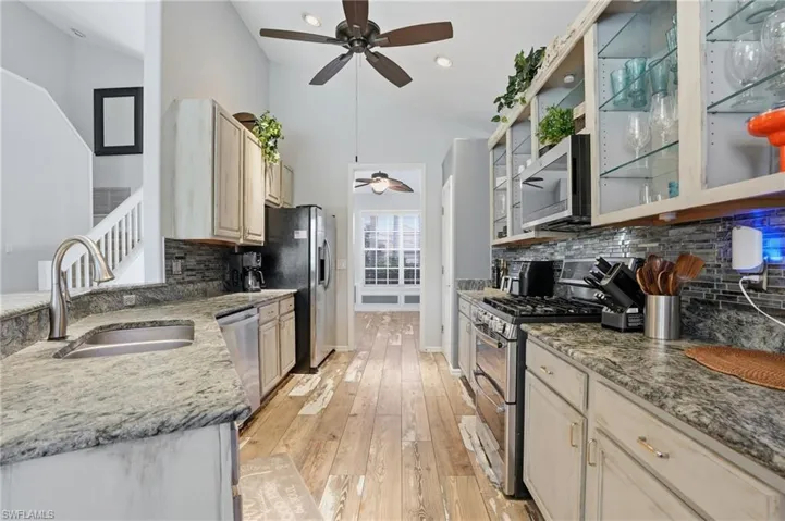 Kitchen featuring vaulted ceiling, stainless steel appliances, glass insert cabinets, light stone counters, and light wood-style flooring