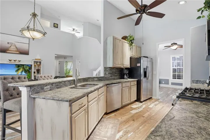 Kitchen featuring light wood finish cabinets, light stone countertops, ceiling fan, open floor plan, and vaulted ceiling