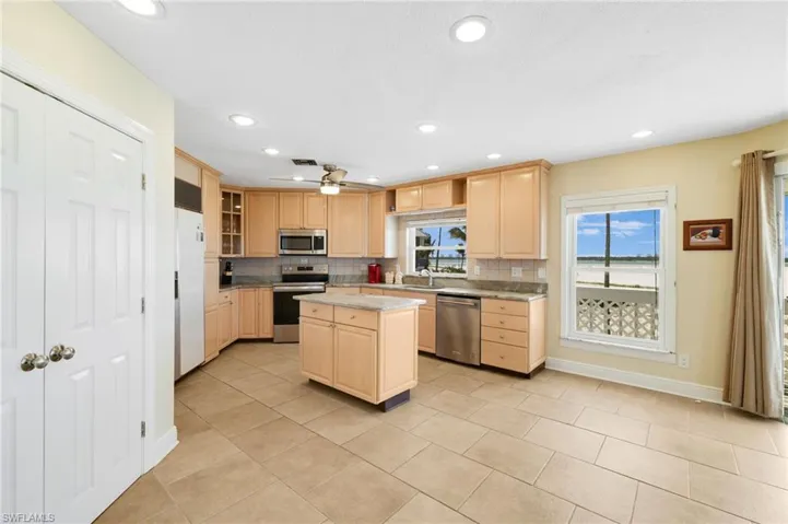 Kitchen featuring light wood-finish cabinetry, stainless steel appliances, a center island with countertop, tile flooring, and recessed lighting - Virtually Edited Image