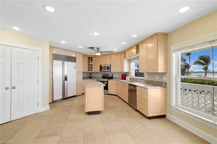 Spacious kitchen featuring light wood cabinetry, stone countertops, stainless steel appliances, and large format tile flooring - Virtually Edited Image