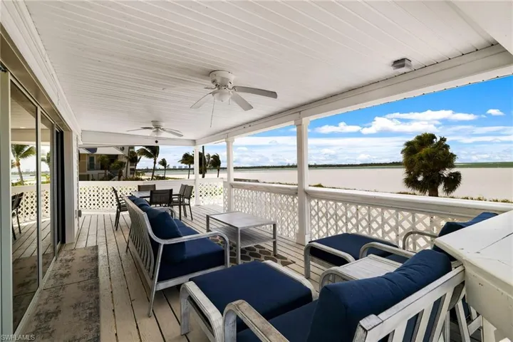 Expansive covered porch featuring white wood-finish flooring, a white wood-paneled ceiling, and multiple ceiling fans - Virtually Edited Image
