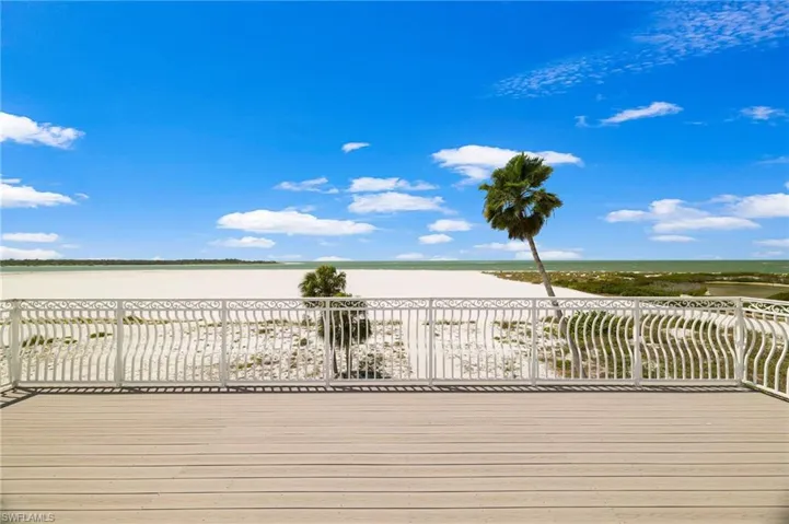 Expansive outdoor decking featuring a decorative white metal railing, beachfront setting, and distant water - Virtually Edited Image