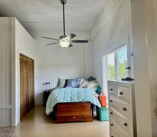 Bedroom with a closet, a ceiling fan, speckled floor, and wood walls