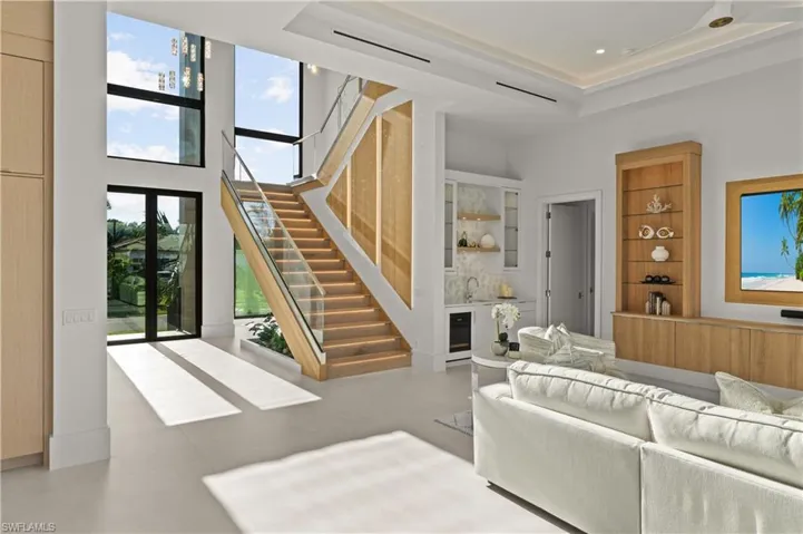Living area with plenty of natural light, bar with sink, a towering ceiling, stairway, and beverage cooler