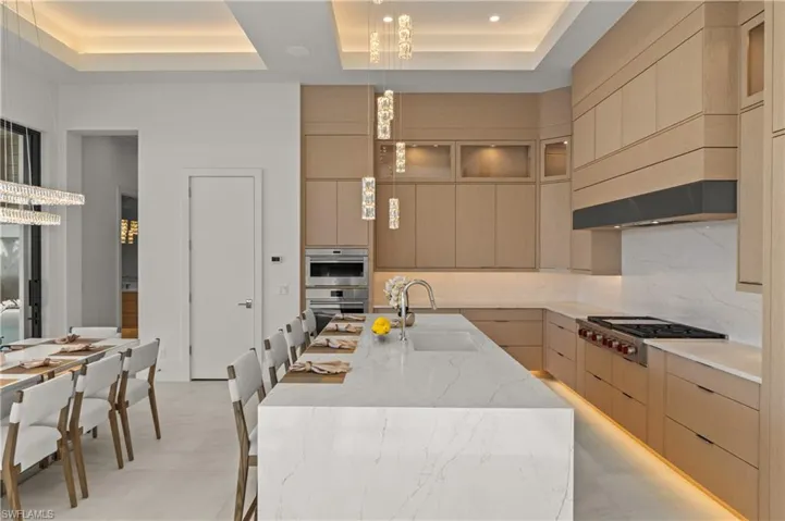 Kitchen with light stone counters, a kitchen bar, decorative light fixtures, backsplash, and a raised ceiling