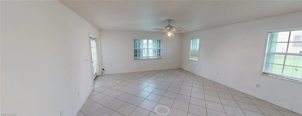 Empty room with ceiling fan, light tile patterned floors, and a healthy amount of sunlight
