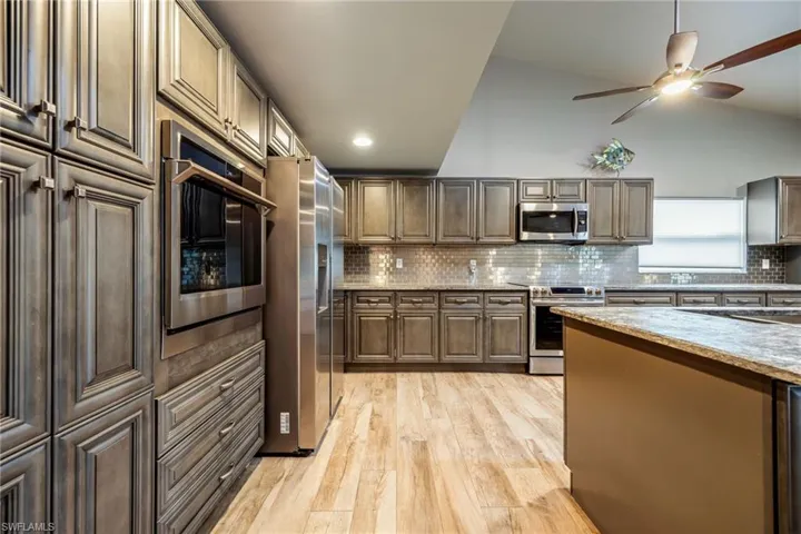Kitchen with appliances with stainless steel finishes, tasteful backsplash, light wood finished floors, ceiling fan, and dark brown cabinets