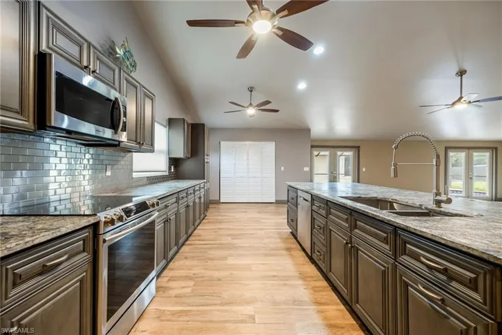 Kitchen with french doors, stainless steel appliances, lofted ceiling, light stone countertops, and recessed lighting