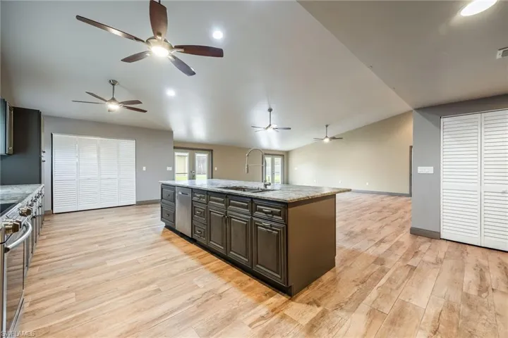 Kitchen with vaulted ceiling, open floor plan, appliances with stainless steel finishes, light stone counters, and a center island with sink