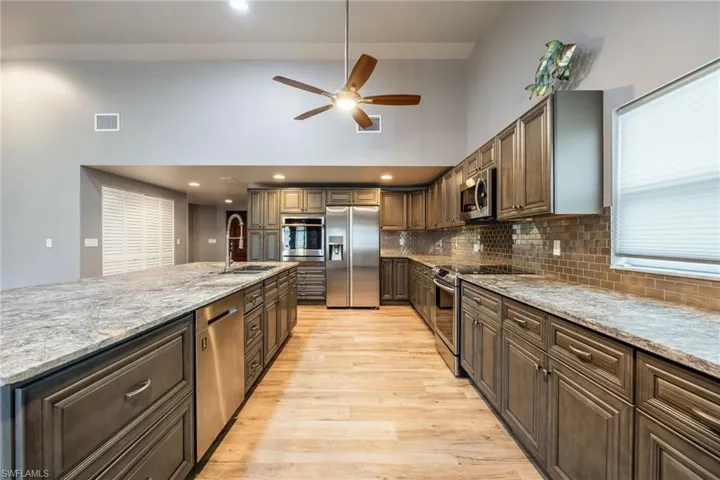 Kitchen with appliances with stainless steel finishes, light stone countertops, tasteful backsplash, light wood-type flooring, and a high ceiling