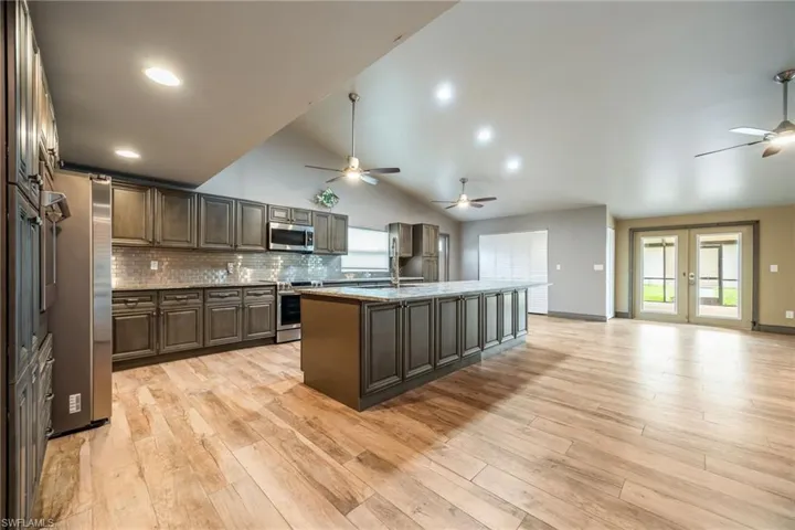 Kitchen featuring tasteful backsplash, appliances with stainless steel finishes, a ceiling fan, light wood finished floors, and high vaulted ceiling