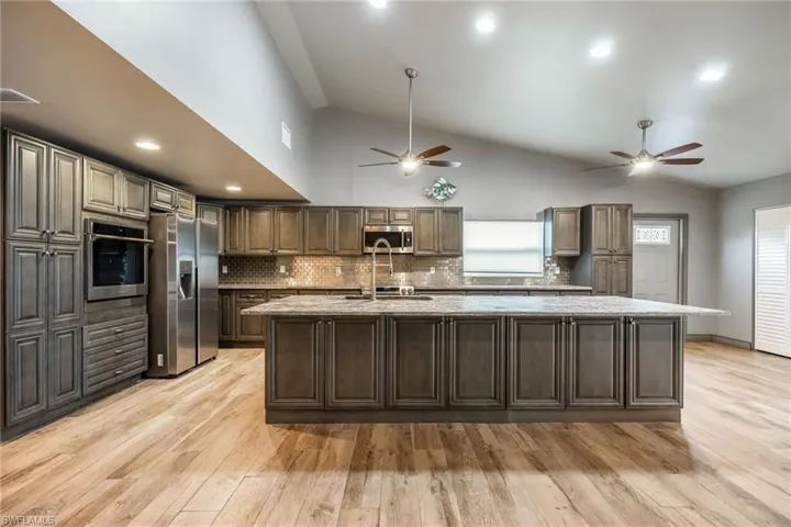 Kitchen with a large island, decorative backsplash, stainless steel appliances, light wood-style floors, and high vaulted ceiling