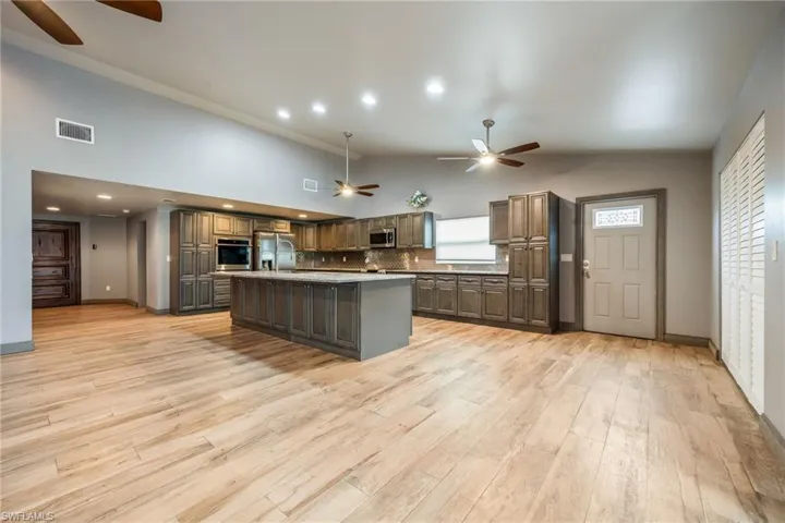 Kitchen featuring ceiling fan, backsplash, stainless steel appliances, a kitchen island, and high vaulted ceiling