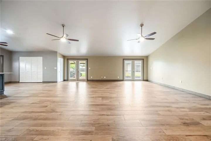 Unfurnished living room featuring french doors, light wood-style floors, a ceiling fan, and lofted ceiling