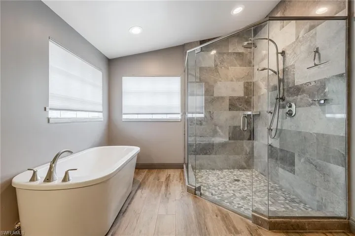 Bathroom with a freestanding bath, a shower stall, light wood-type flooring, and vaulted ceiling