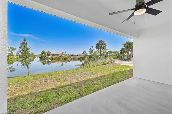 View of green lawn with a water view, ceiling fan, and a patio